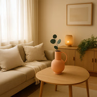 A soft beige living room with a wooden table displaying a peach vase with greenery creating a warm minimal decor scene with gentle natural daylight.