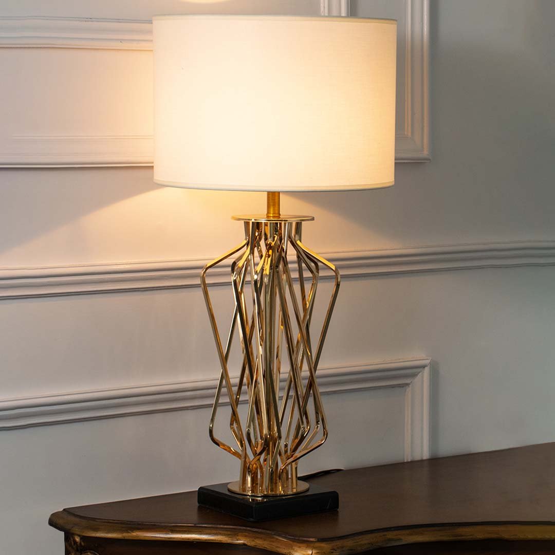 Gold metal geometric table lamp with fabric drum shade offering luxury decor appeal and warm ambient lighting indoors.