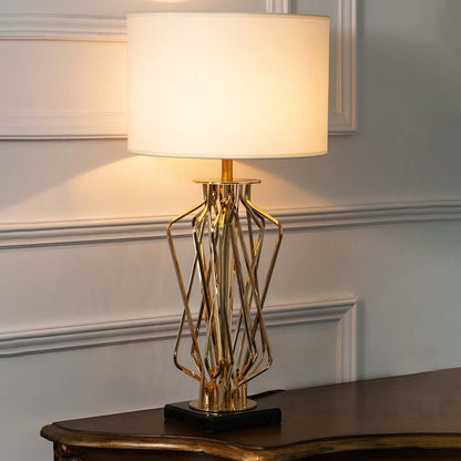 Gold metal geometric table lamp with fabric drum shade offering luxury decor appeal and warm ambient lighting indoors.
