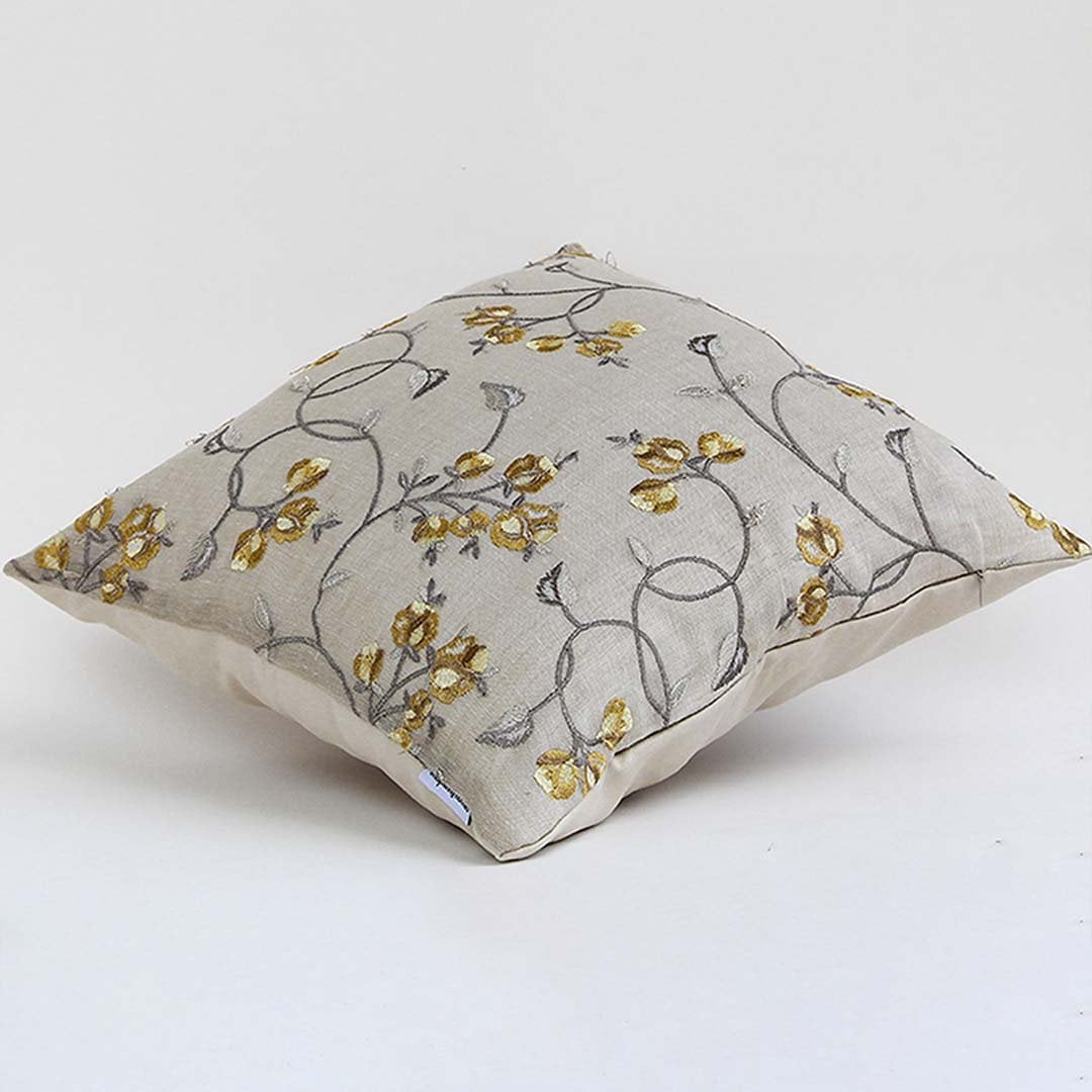 Beige cotton cushion cover with yellow floral embroidery displayed at an angle offering a natural artistic décor look with a breathable soft and skin friendly fabric finish.