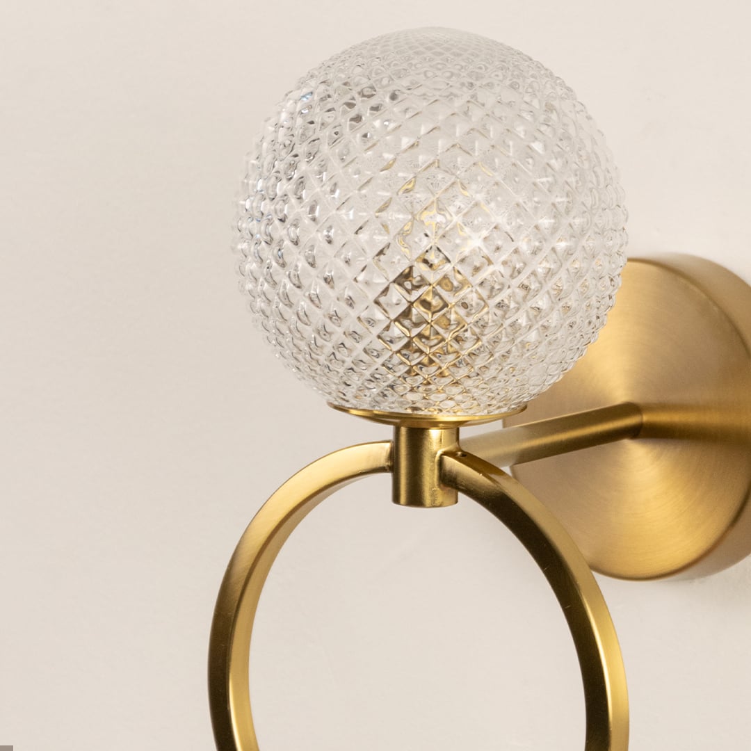A closeup of the gold ring wall light highlighting the faceted glass globe and smooth brushed metal ring for a refined modern decorative finish.
