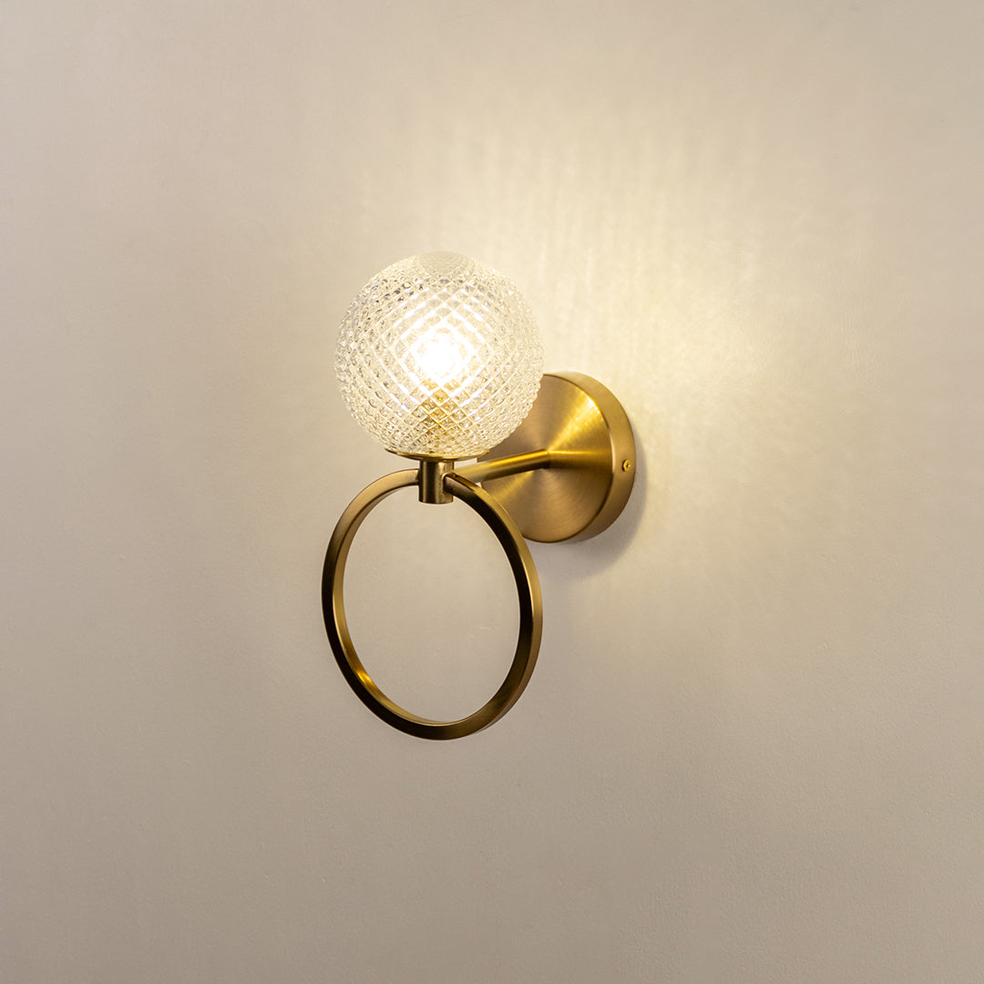 Gold finish wall light with textured glass shade emitting warm glow perfect for bedroom hallway wall decor on clean white background.