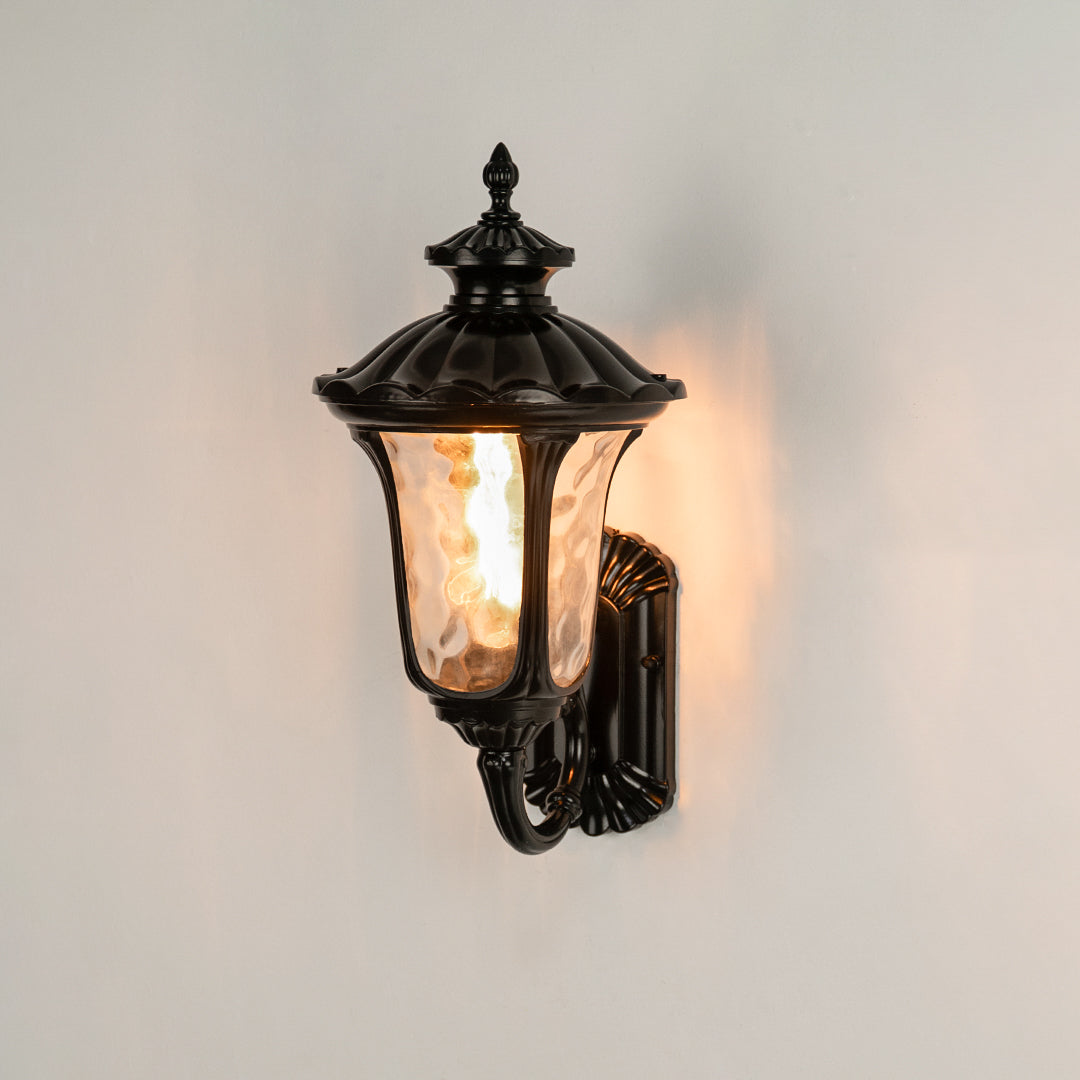 Black metal outdoor wall lantern on white background with textured water glass shade for classic entryway decor.