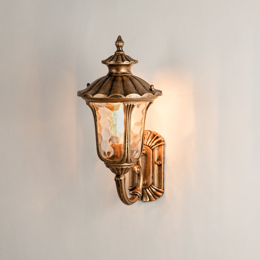 Antique brass outdoor wall lantern on white background with textured water glass shade for traditional porch decor.