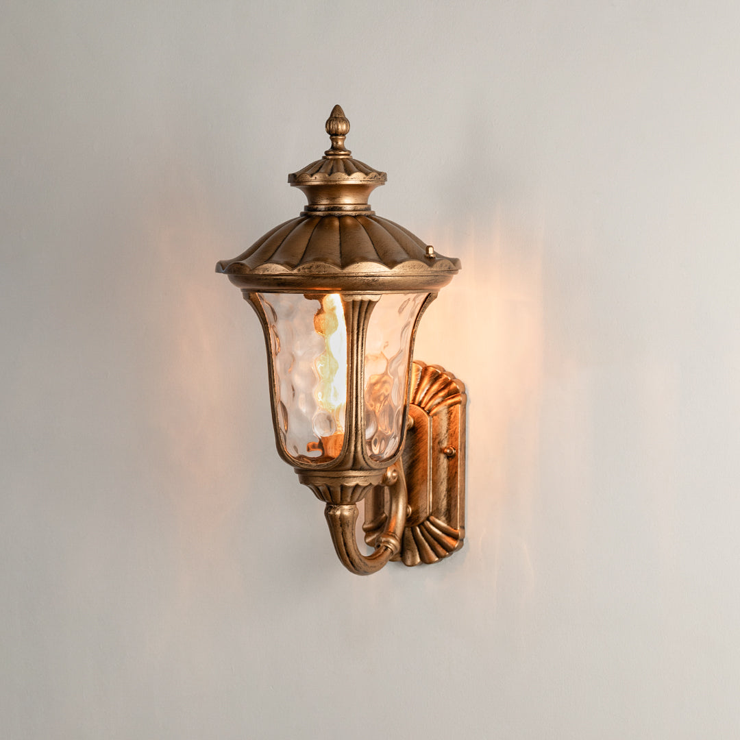 Antique brass outdoor wall light on white background with textured water glass shade for traditional porch decor.