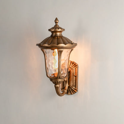 Antique brass outdoor wall light on white background with textured water glass shade for traditional porch decor.