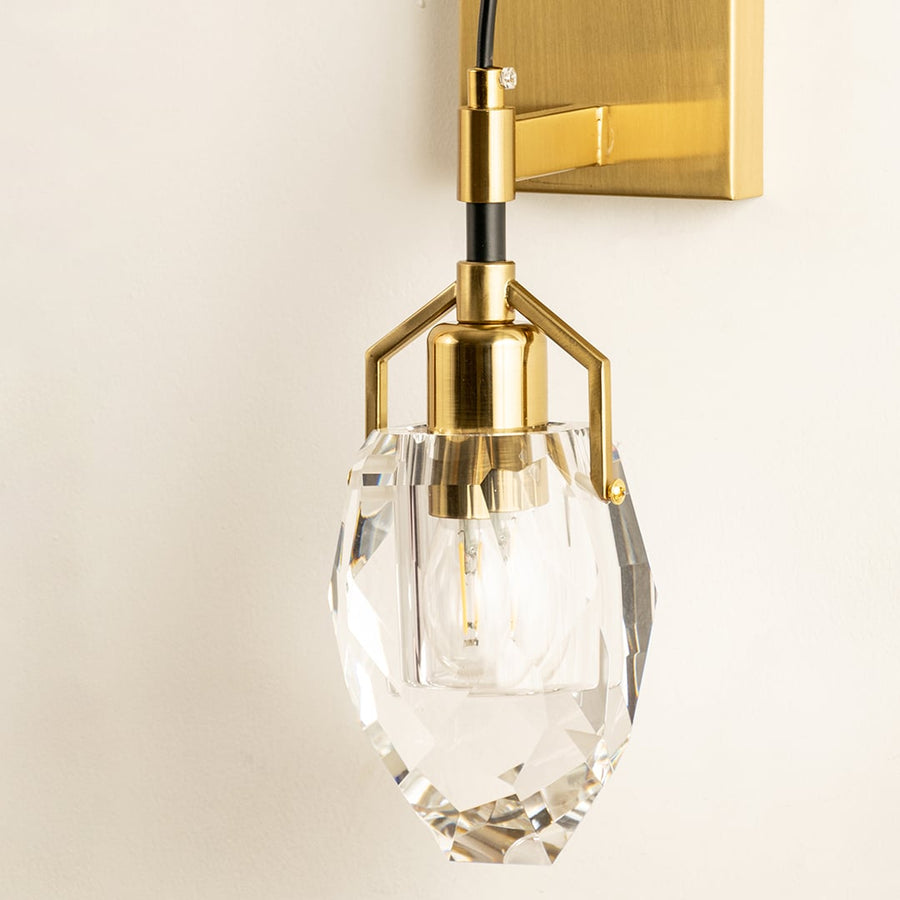 A gold and glass wall light with a sculpted shade glowing on a beige wall providing warm illumination and refined contemporary interior décor.