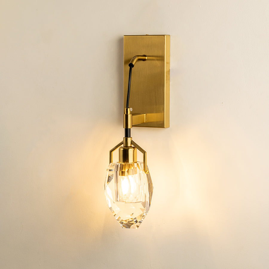 Gold metal wall light with clear glass shade emitting warm glow perfect for elegant interior wall decor styling.