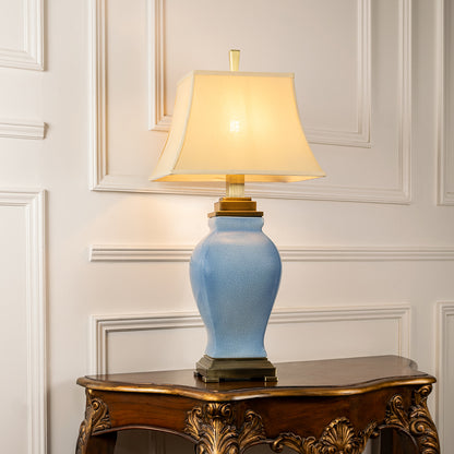 Light blue ceramic table lamp with fabric shade placed on a carved console table creating refined traditional lighting.