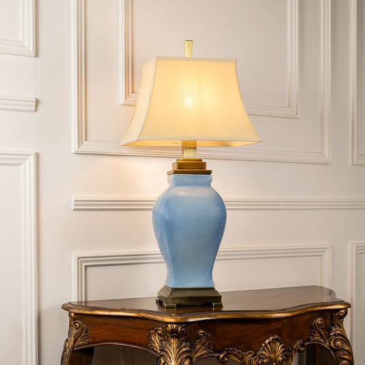 Light blue ceramic table lamp with fabric shade placed on a carved console table creating refined traditional lighting.