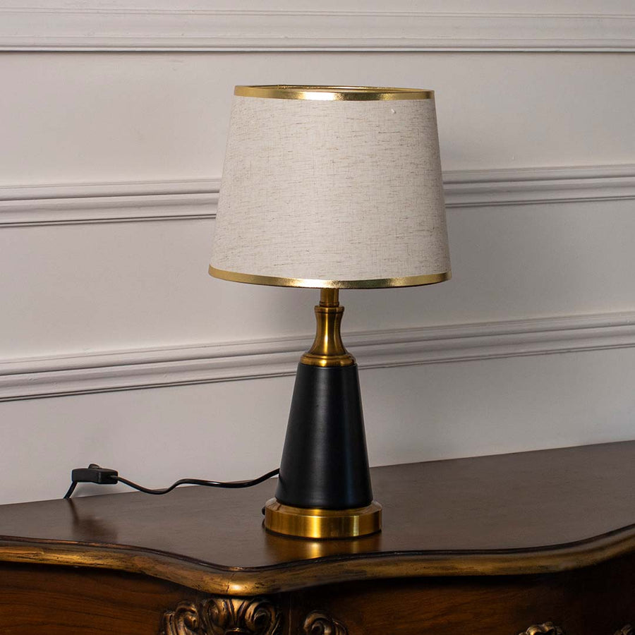 Contemporary table lamp with linen shade and gold-trimmed black base placed against a white background for a clean look.