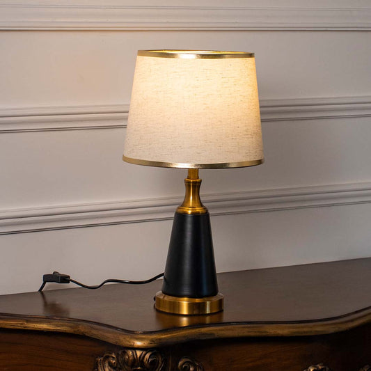 Black ceramic table lamp with cream fabric shade casting warm ambient light for sophisticated bedside table decor.