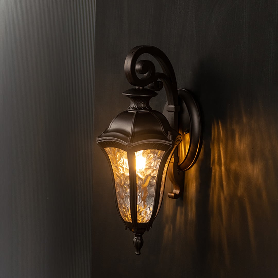 Lantern style wall light radiating warm glow highlights its intricate design against a black background.