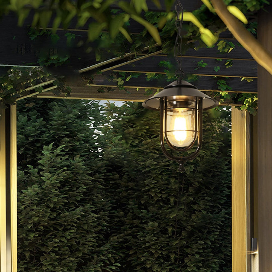 A classic outdoor lantern hanging above a rustic patio with lush green plants and wooden structures creating a calm and inviting outdoor setting.
