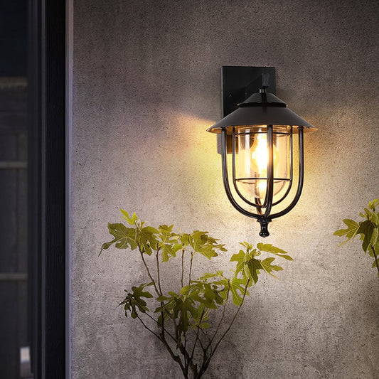 Black outdoor wall lantern styled in a soft lifestyle setting showing its curved metal frame and clear glass shade for an elegant exterior look.