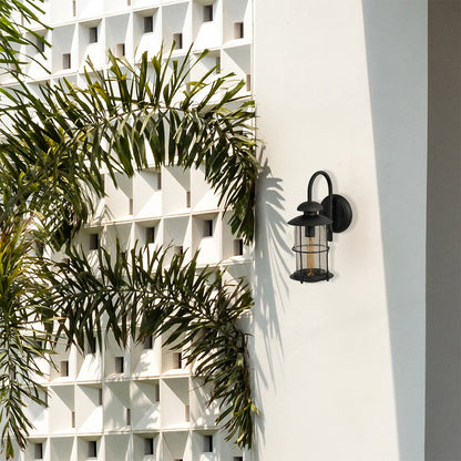 Modern black outdoor lantern styled in a minimal setting showing its clear raindrop glass and elegant curved arm shape.