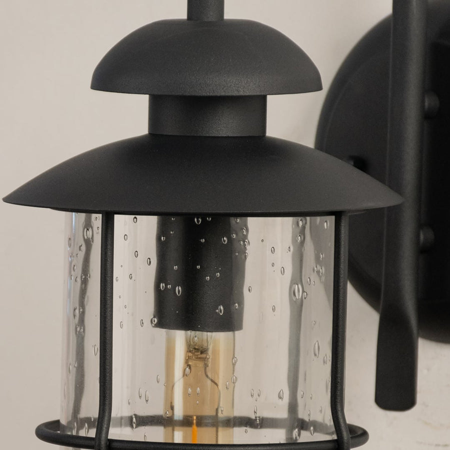 Closeup view of the black outdoor lantern showing the raindrop textured glass and sleek curved arm in fine detail.