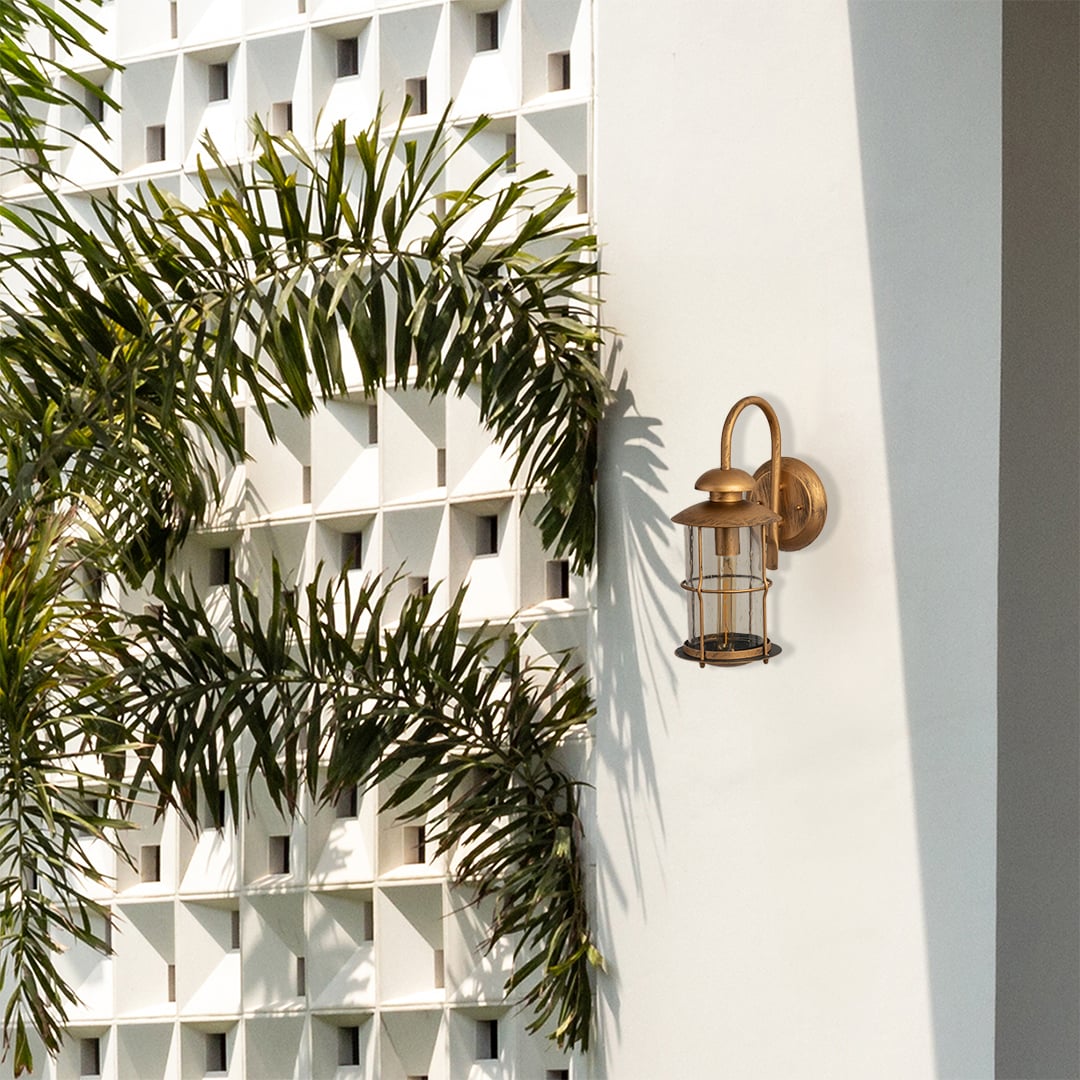 Industrial brass gooseneck outdoor wall sconce lifestyle image mounted on a white modern villa wall alongside palm trees.