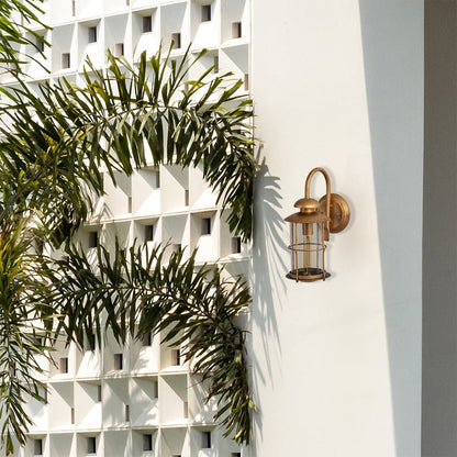 Industrial brass gooseneck outdoor wall sconce lifestyle image mounted on a white modern villa wall alongside palm trees.