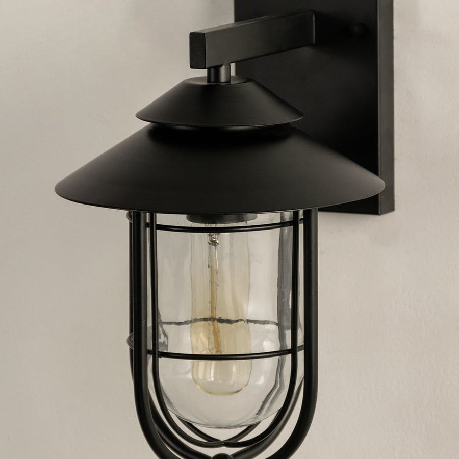 A detailed close view of the black outdoor wall light showcasing its curved metal frame glass enclosure and refined finish capturing the overall craftsmanship.