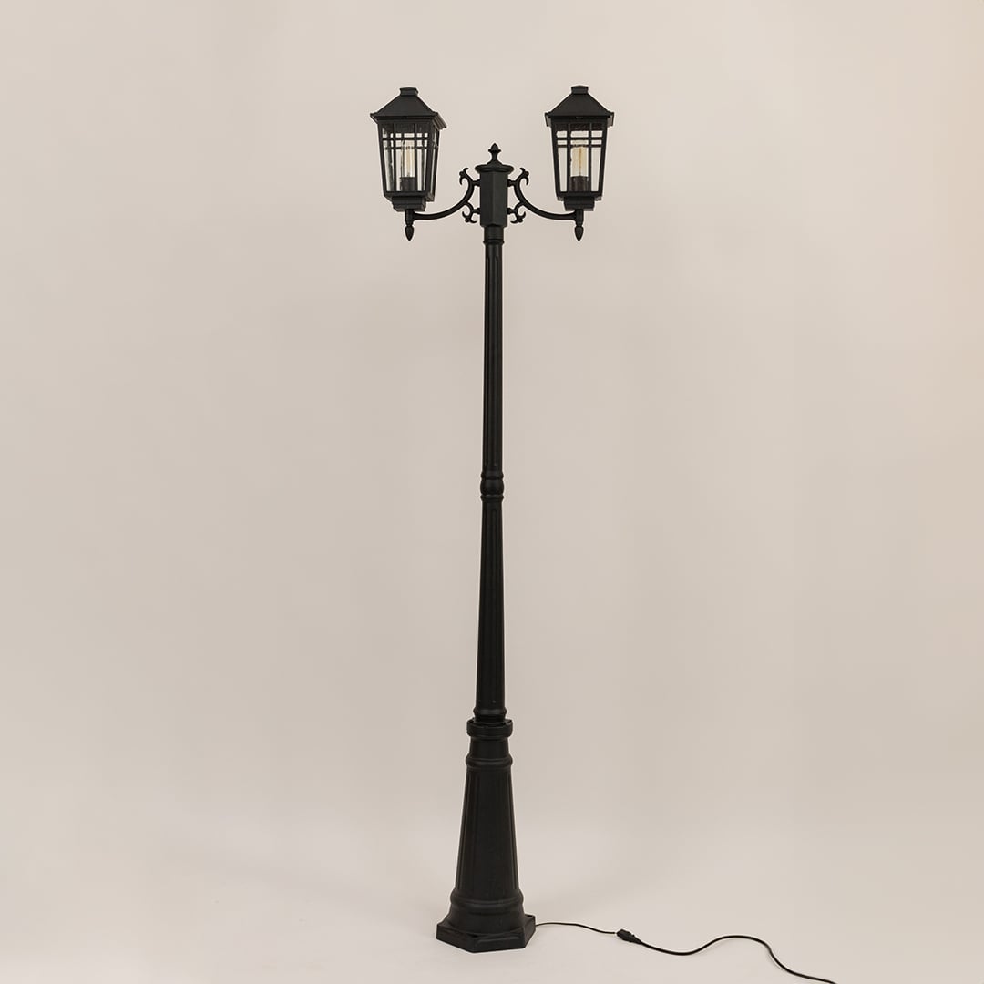 Classic black twin head post light with lantern style fixtures and tall decorative pole switched off on white backdrop.