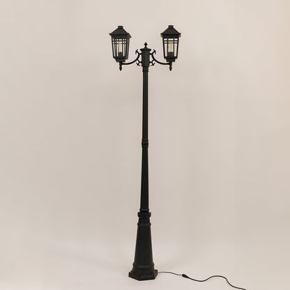 Classic black twin head post light with lantern style fixtures and tall decorative pole switched off on white backdrop.
