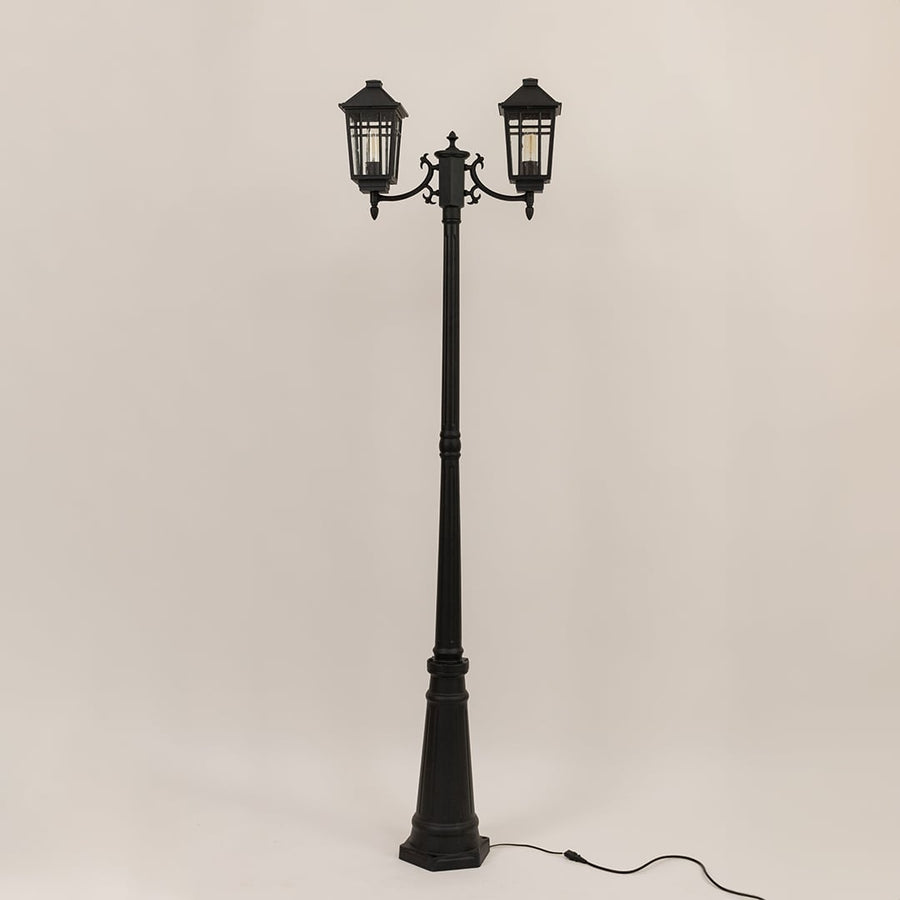 Classic black twin head post light with lantern style fixtures and tall decorative pole switched off on white backdrop.