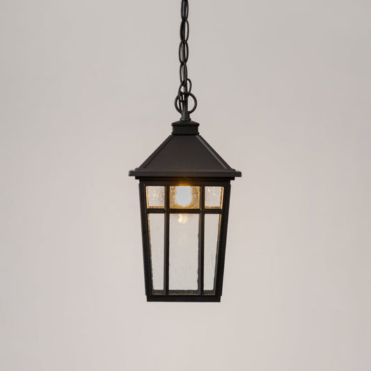 Illuminated black metal hanging lantern with clear glass panels and warm LED bulb glowing on clean white background.
