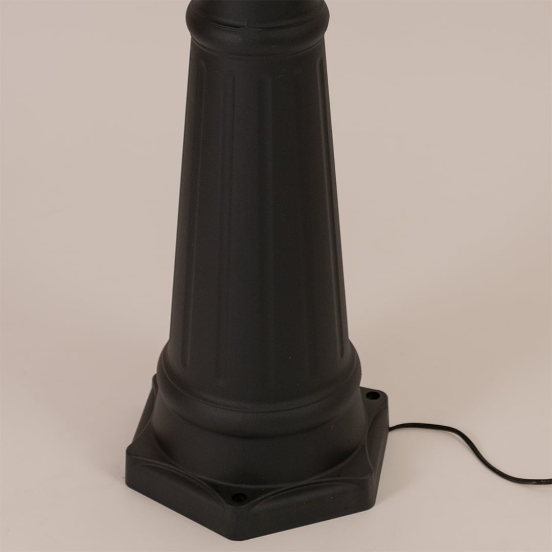 Detailed close up of black metal post lamp base showing textured pole construction and decorative mounting foundation design.