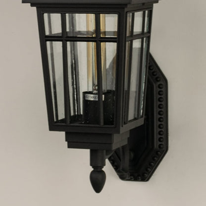 Closeup of a black outdoor lantern showing warm light shining through clear glass panels revealing textured reflections and classic lantern craftsmanship.