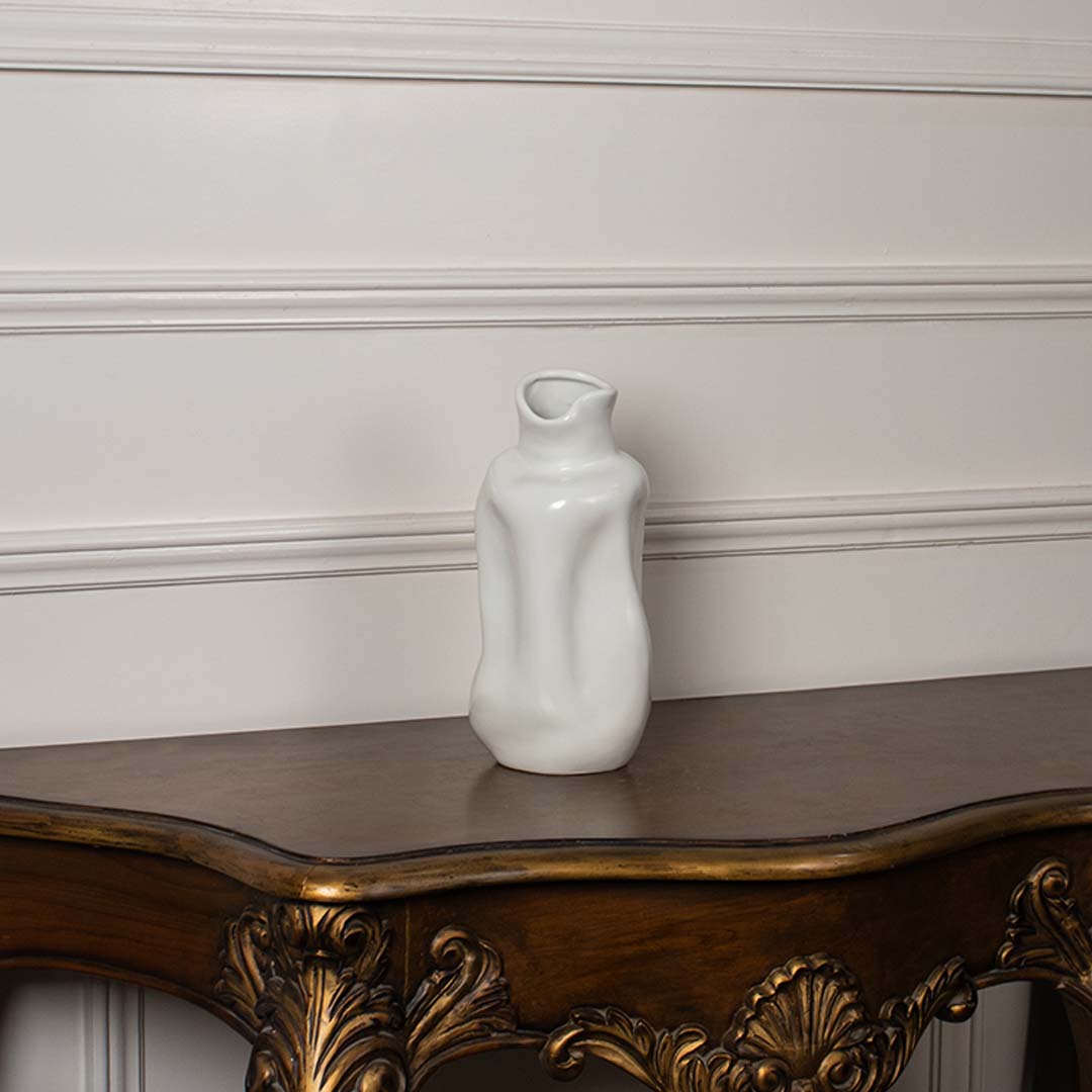 Glossy white ceramic vase with organic fluid wave shapes displayed on a vintage wood console table for luxury decor.