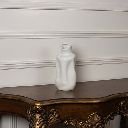 Glossy white ceramic vase with organic fluid wave shapes displayed on a vintage wood console table for luxury decor.