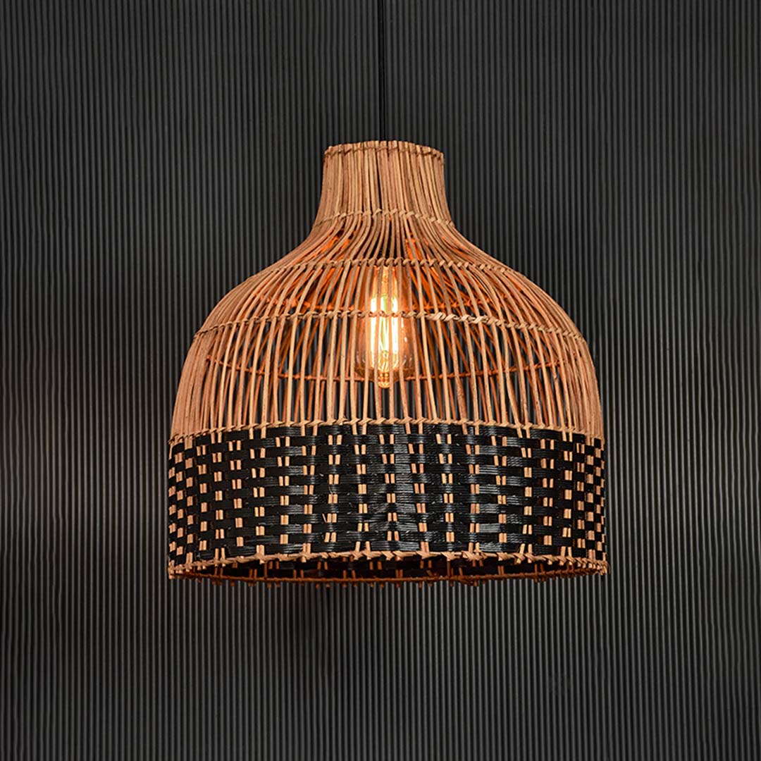 Rattan pendant light illuminated on black background radiating a warm glow through its two-tone woven design.