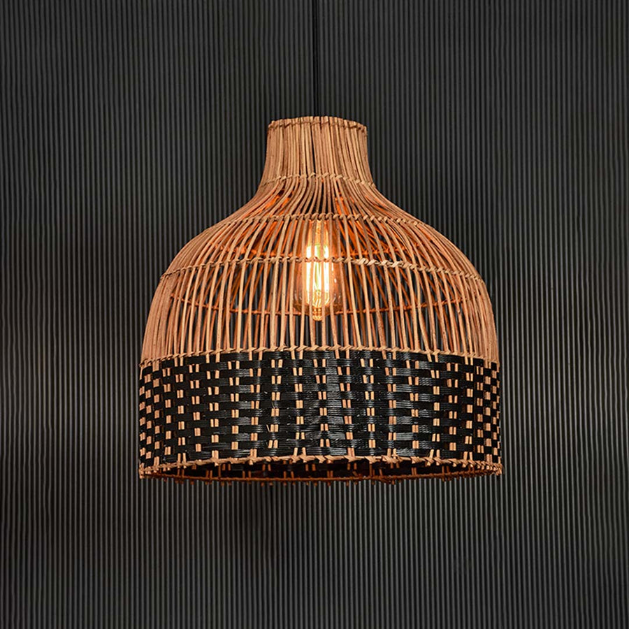 Rattan pendant light illuminated on black background radiating a warm glow through its two-tone woven design.