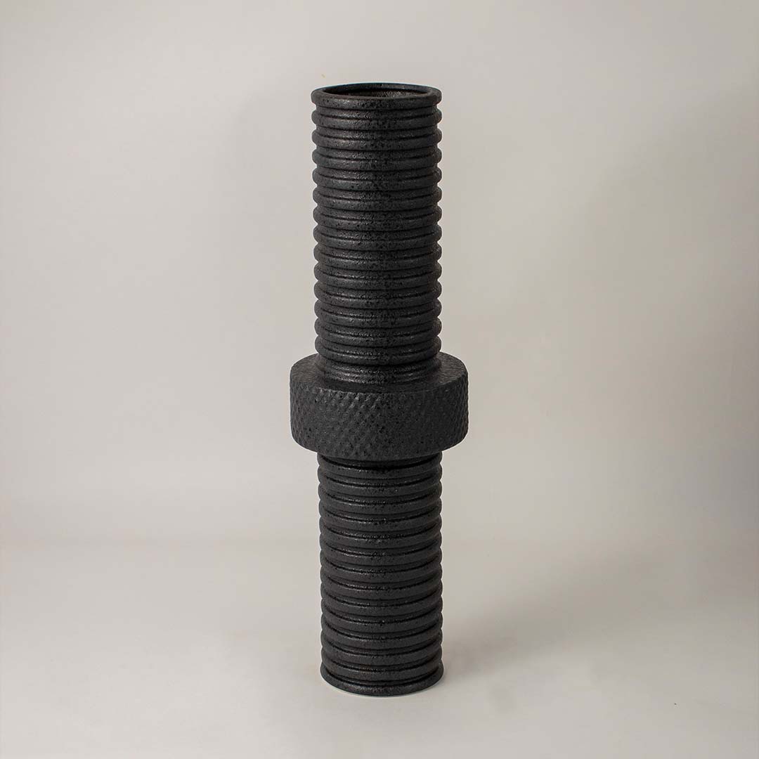Matte black metal vase highlighted under soft lighting on white background enhancing its bold industrial texture appeal.