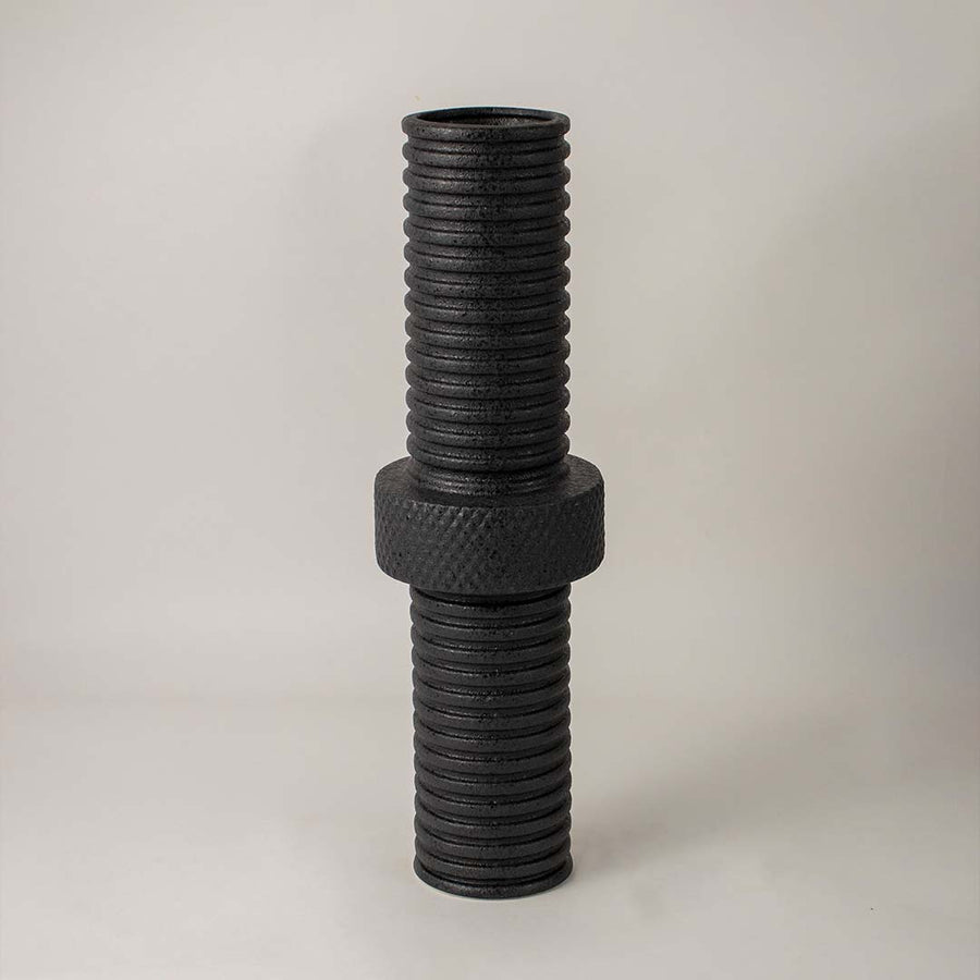 Matte black metal vase highlighted under soft lighting on white background enhancing its bold industrial texture appeal.