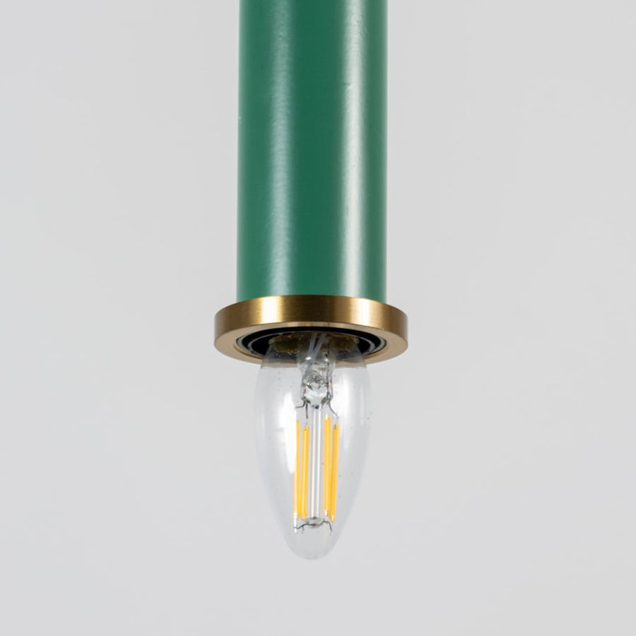 Closeup of green pendant light with brass ring and clear bulb turned on showing elegant ceiling decor detail.