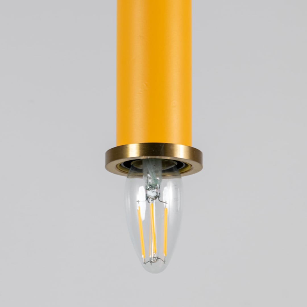 Closeup of yellow pendant light with brass ring and clear bulb turned on showing detailed ceiling decor design.