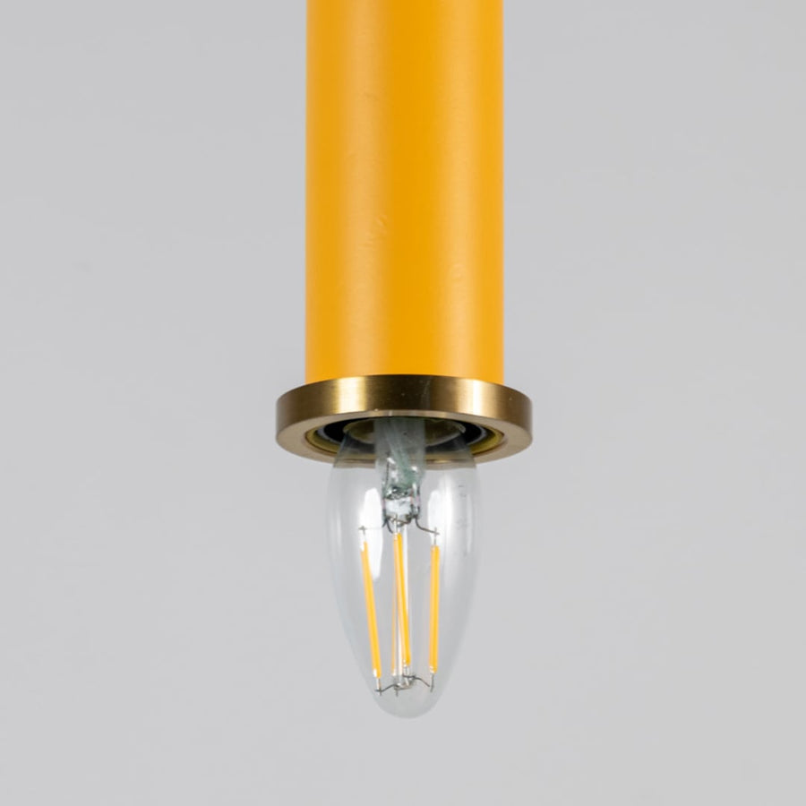 Closeup of yellow pendant light with brass ring and clear bulb turned on showing detailed ceiling decor design.