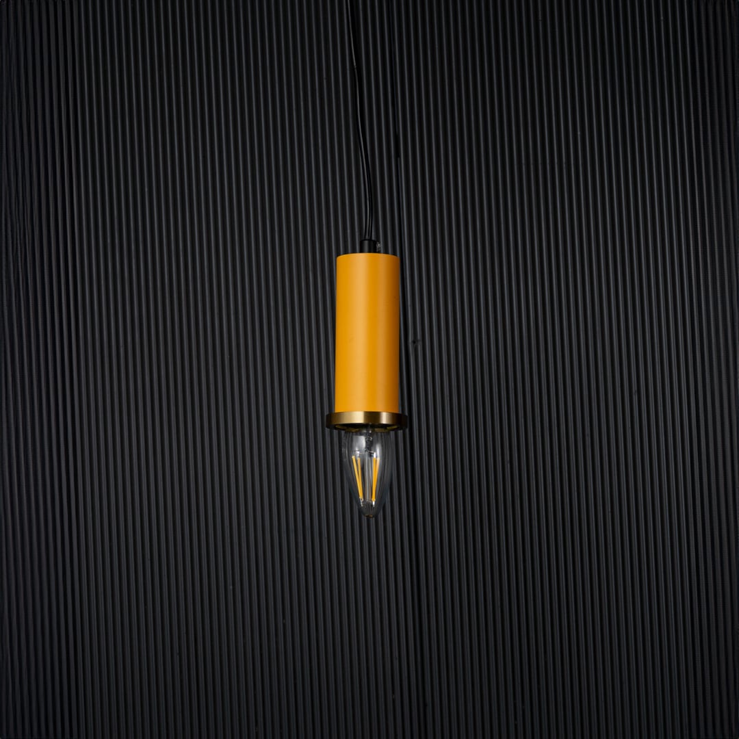 Yellow pendant light turned off with brass accent and bulb shown as modern hanging decor on black background.
