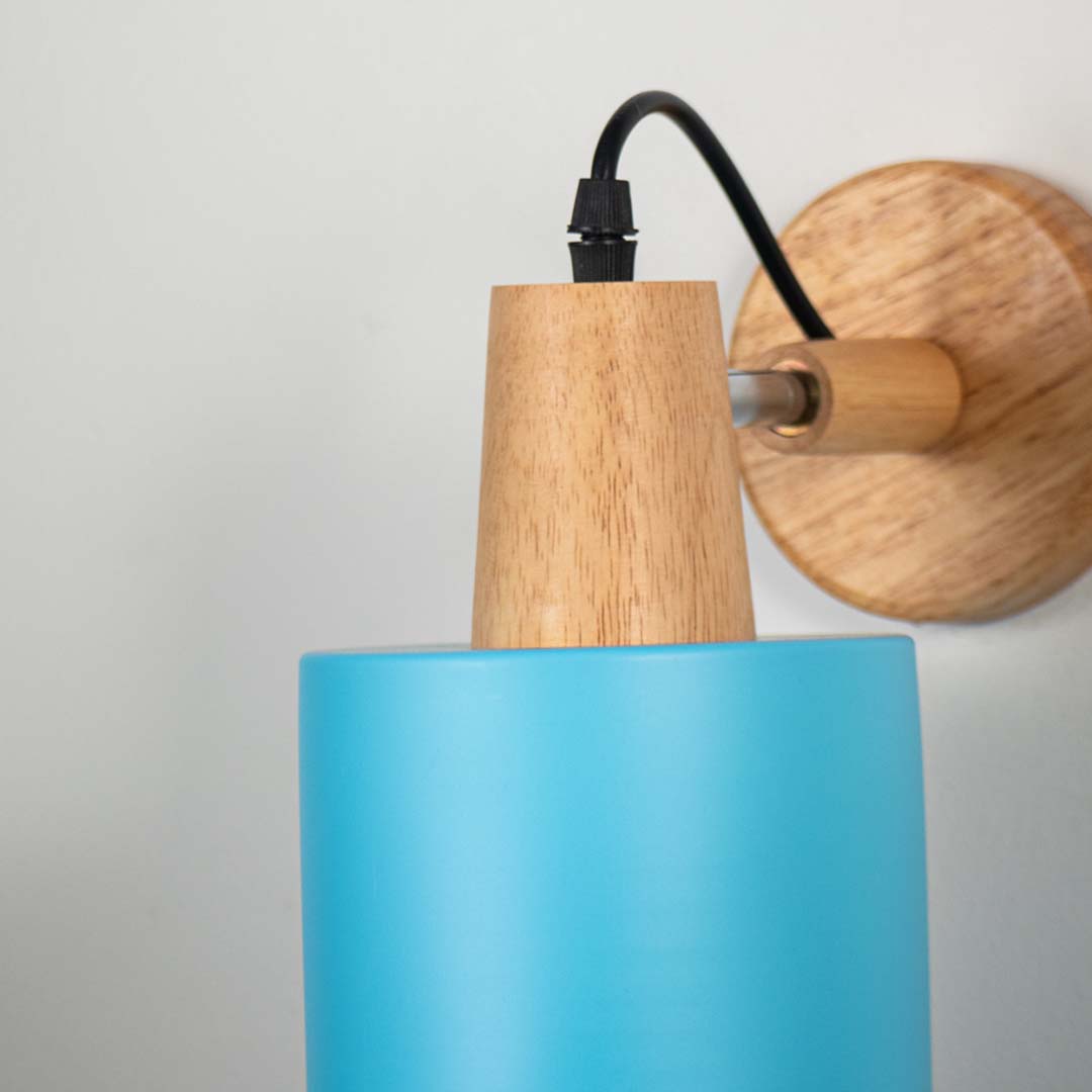 Closeup of modern wall lamp with matte sky blue cylinder shade wooden base and black cord showcasing elegant wall lighting design.