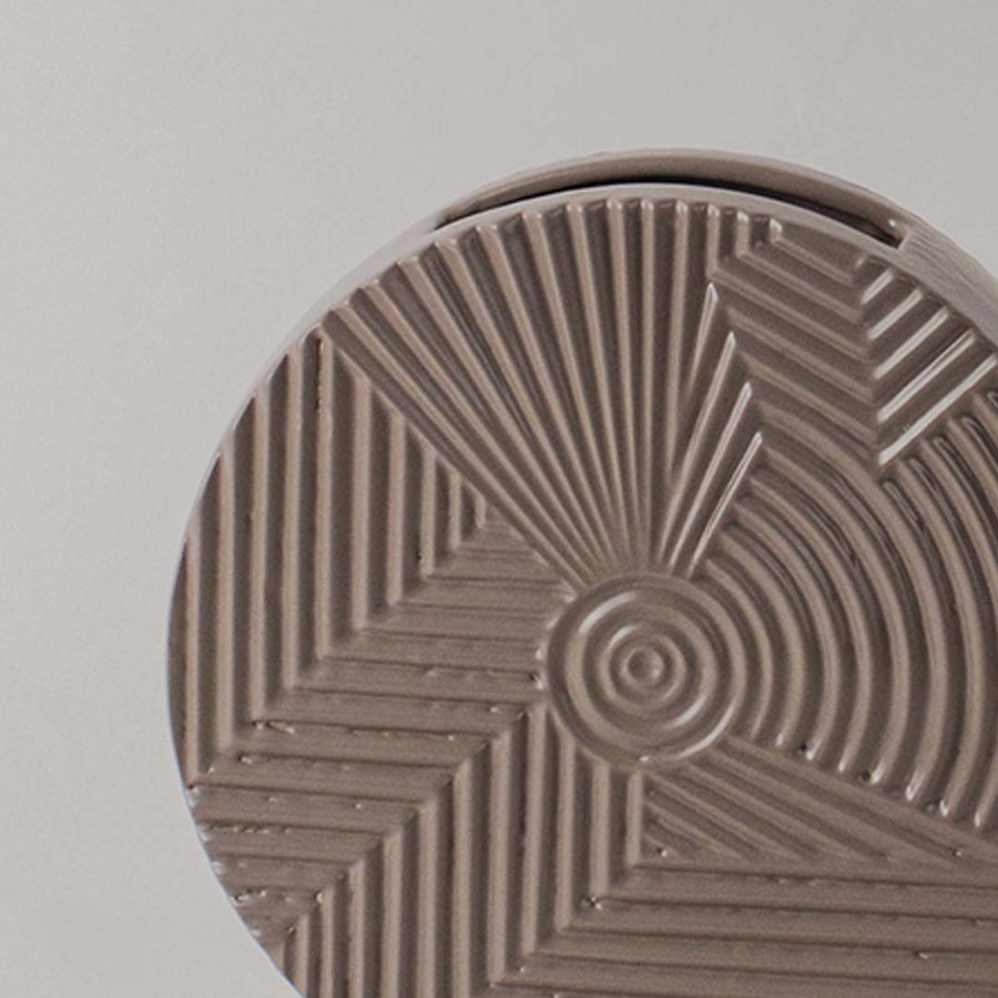 Detailed closeup view of the engraved geometric lines and central spiral pattern on the brown ceramic vase surface.