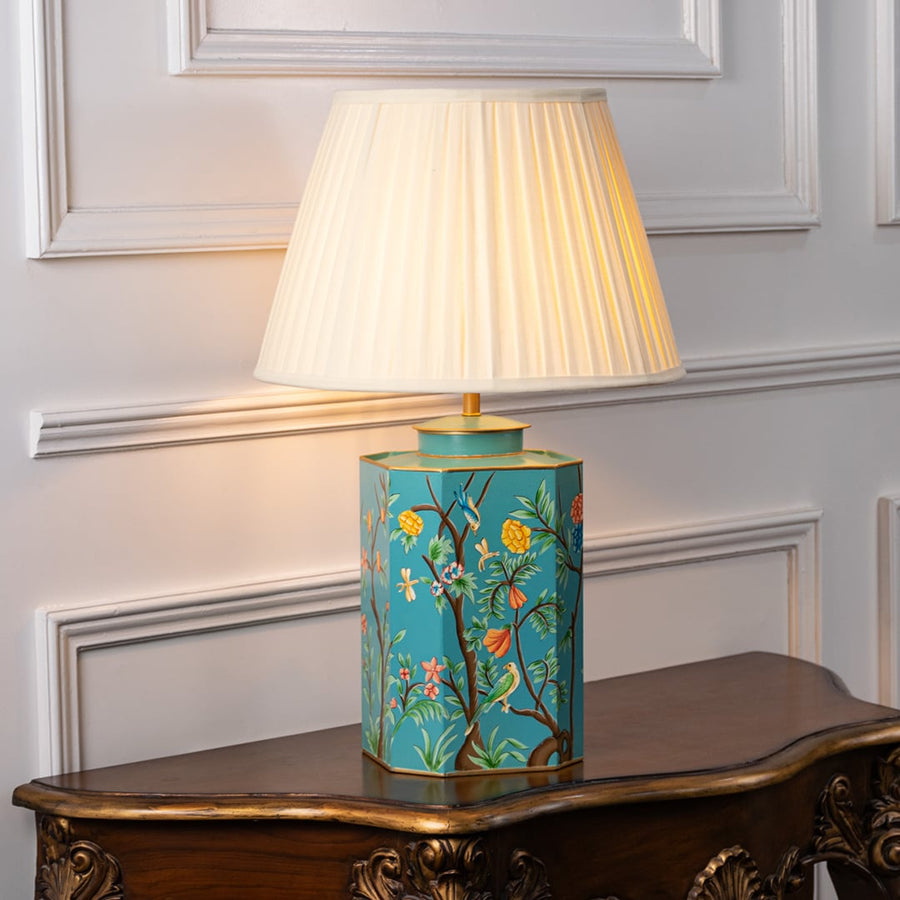 Decorative table lamp with pleated white shade and turquoise ceramic base detailed with floral artwork and gold accents for home decor.