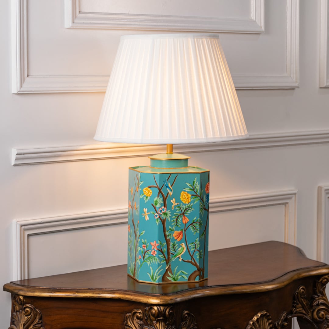 Table lamp showcasing white fabric shade with teal floral ceramic base and gold detailing styled on elegant wooden console.