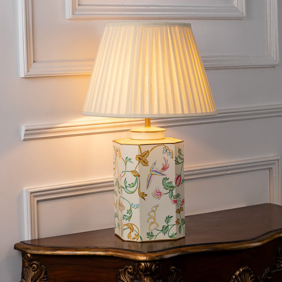 Table lamp on white background featuring hand painted floral ceramic base with soft pleated shade creating warm elegant lighting.