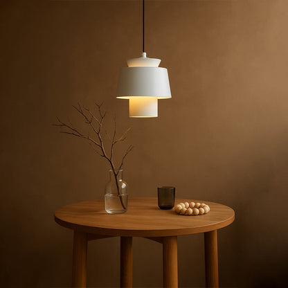 A modern white pendant lamp glows warmly above a wooden table creating a soft ambient scene with minimalist decor and a calm earthy interior setting.