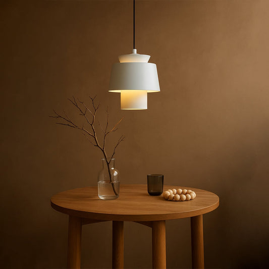 A modern white pendant lamp glows warmly above a wooden table creating a soft ambient scene with minimalist decor and a calm earthy interior setting.