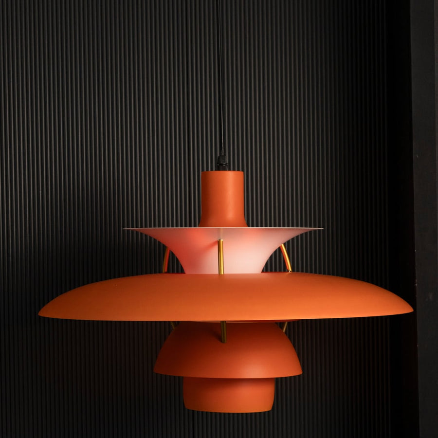 Orange metal pendant light switched on against black background creating warm focused illumination for modern dining interiors.
