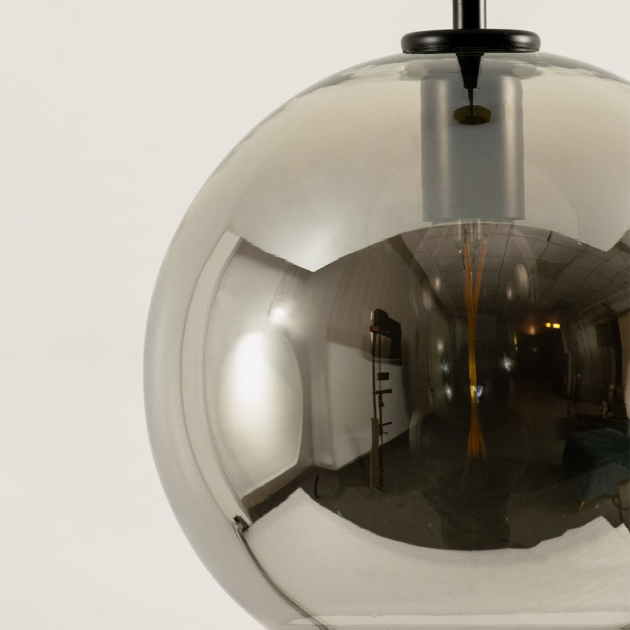 Closeup of smoked glass pendant light with globe design and black suspension rod stylish ceiling lamp for modern home interiors.