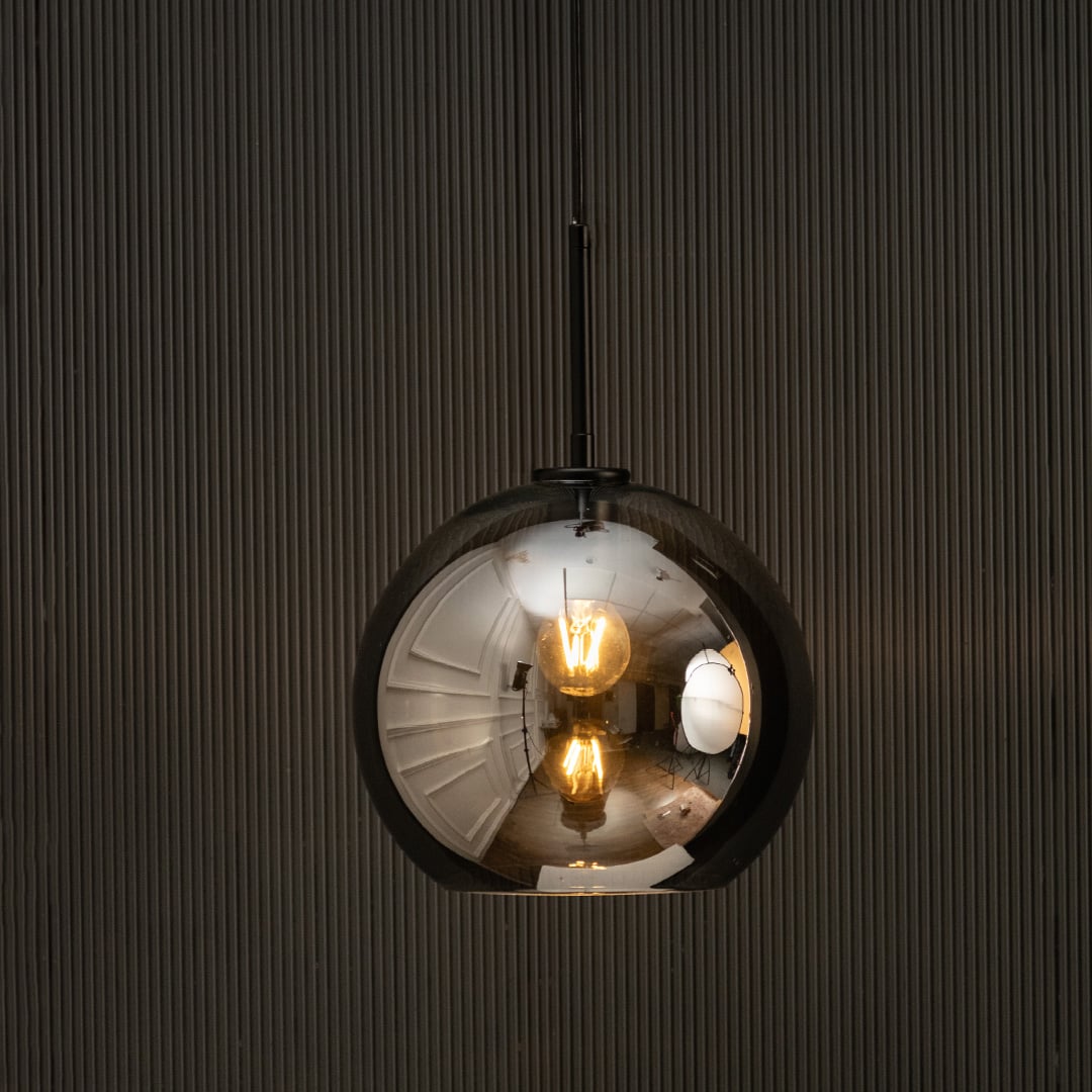 Smoked glass globe pendant light glowing on black background with warm filament bulbs creating moody modern interior lighting.